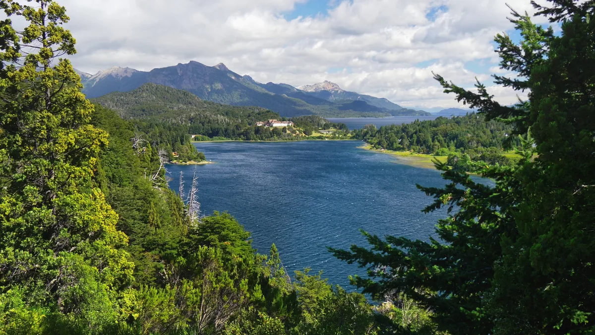Vista do lago Nahuel Huapi a partir do Punto Panorámico, com a península coberta de mata e a cordilheira nevada ao fundo