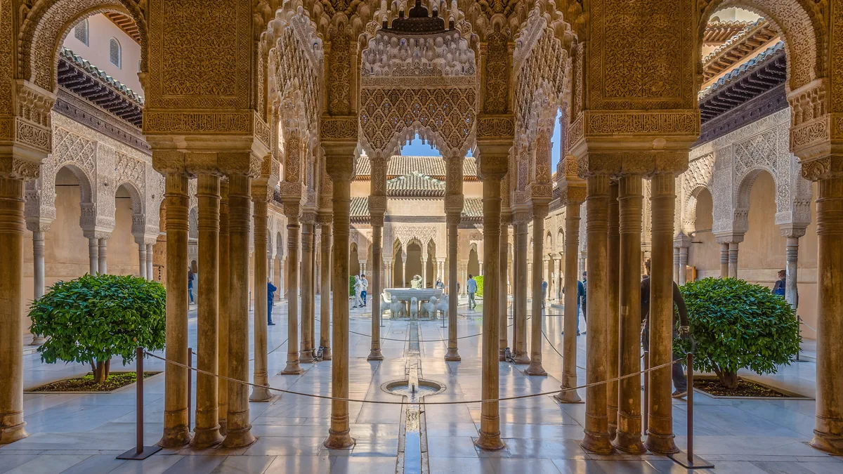 O Pátio dos Leões da Alhambra visto por entre a arcada, com as colunas finas e a fonte ao centro