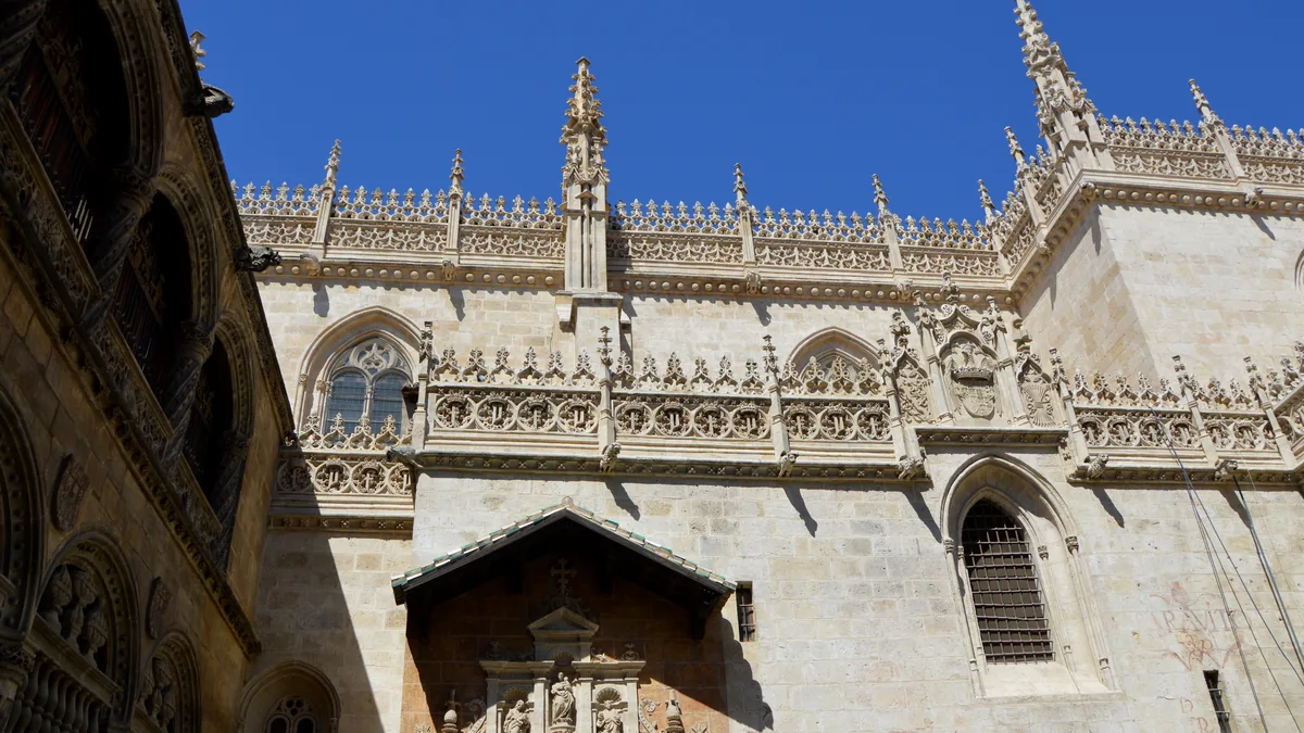 A fachada gótica da Capilla Real de Granada, com os pináculos e a balaustrada rendilhada contra o céu azul
