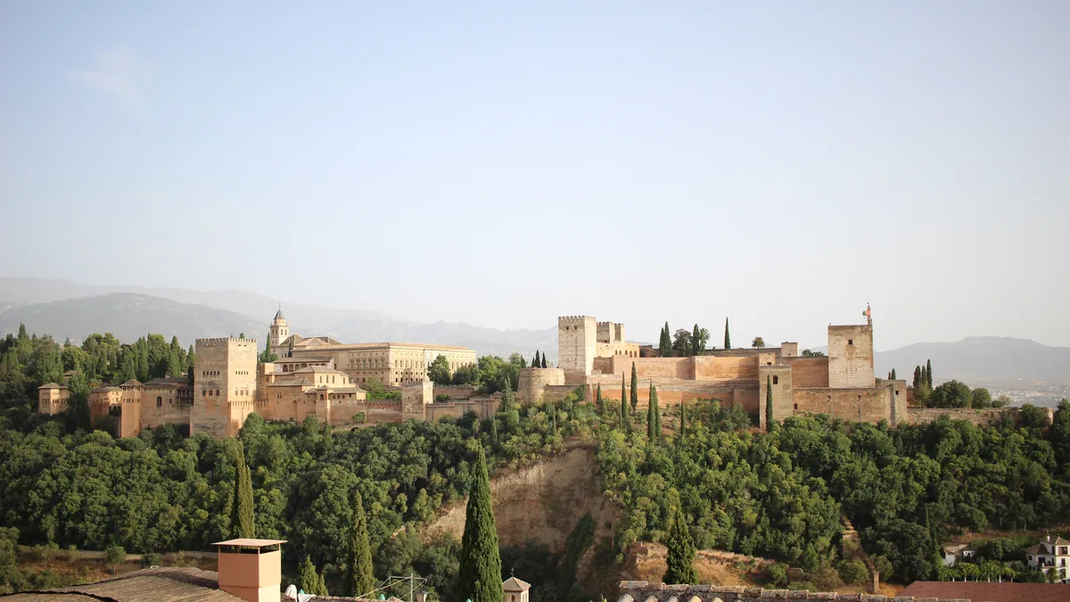 A Alhambra vista de longe do outro lado do vale, com o arvoredo à frente e a serra ao fundo