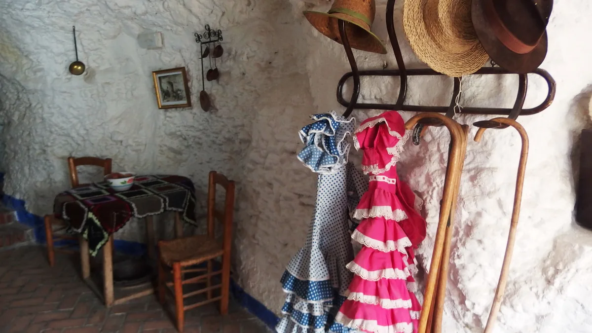 O interior de uma caverna do Museo Cuevas del Sacromonte, com paredes caiadas, mesa posta e vestidos de flamenco pendurados