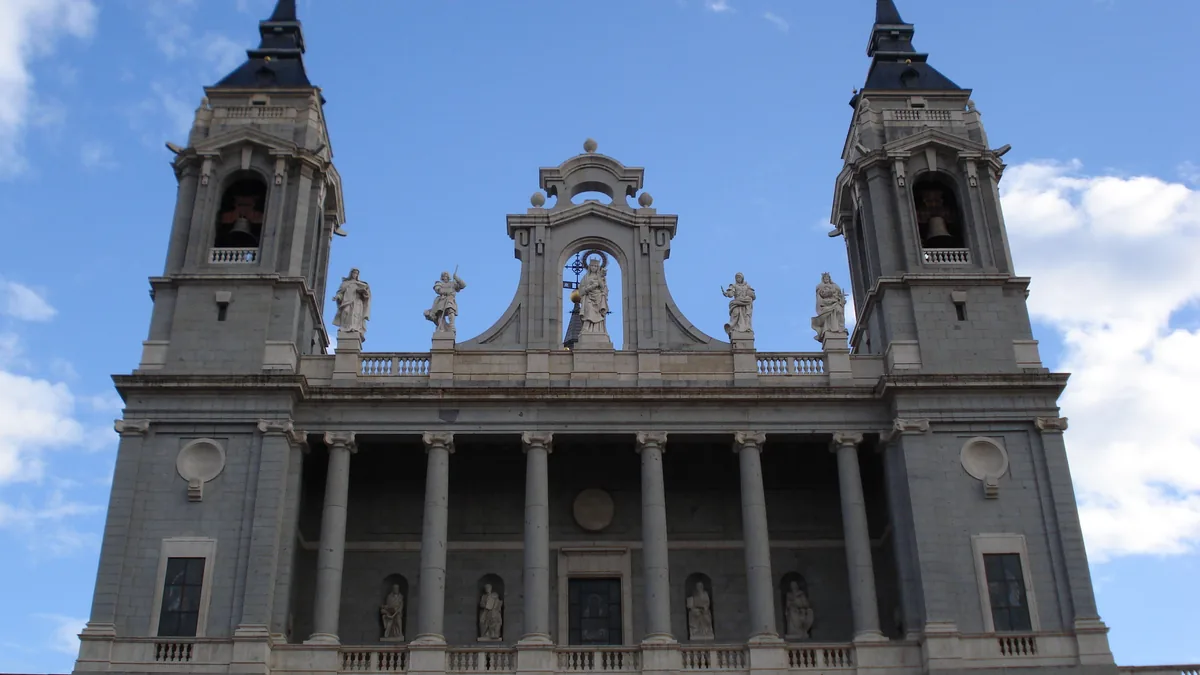 A fachada principal da Catedral de la Almudena, com as duas torres sineiras e o pórtico central de pedra clara contra o céu azul