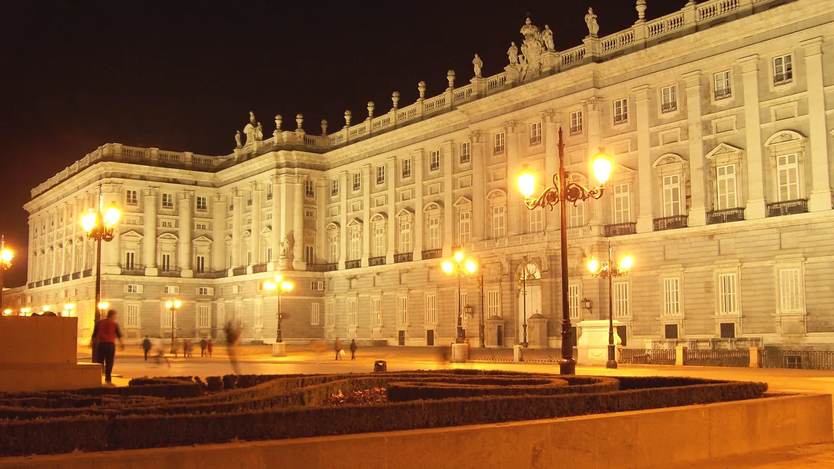 A fachada do Palácio Real de Madri iluminada à noite, vista da Plaza de Oriente, com as luminárias acesas no largo em frente
