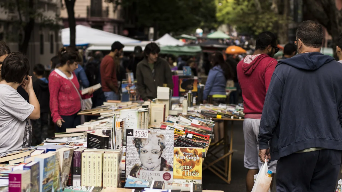 Banca de livros usados na Feria de Tristán Narvaja, em Montevidéu, com pessoas folheando e barracas ao fundo