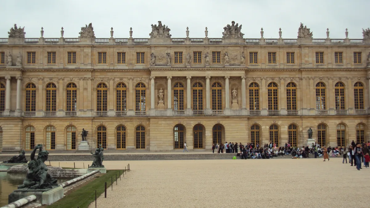 A fachada oeste do Palácio de Versalhes vista do parterre, com as estátuas do jardim e o público no pátio