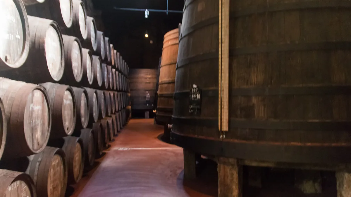 Fileiras de barris de vinho do Porto empilhados numa cave de Vila Nova de Gaia, sob luz baixa