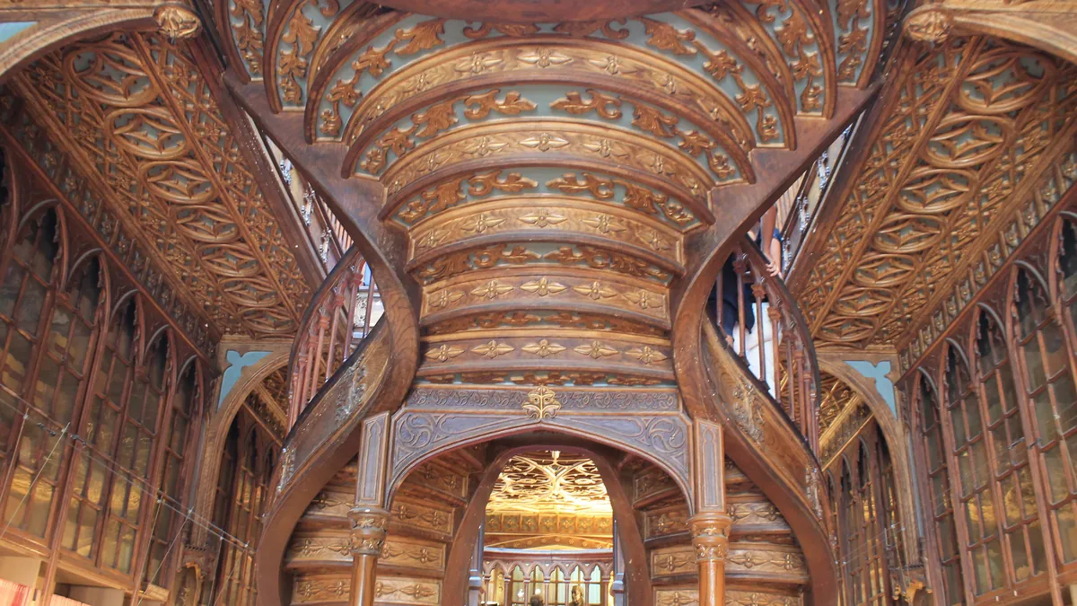 Teto de madeira entalhada da Livraria Lello visto de baixo, com a galeria do piso superior e o vitral ao fundo
