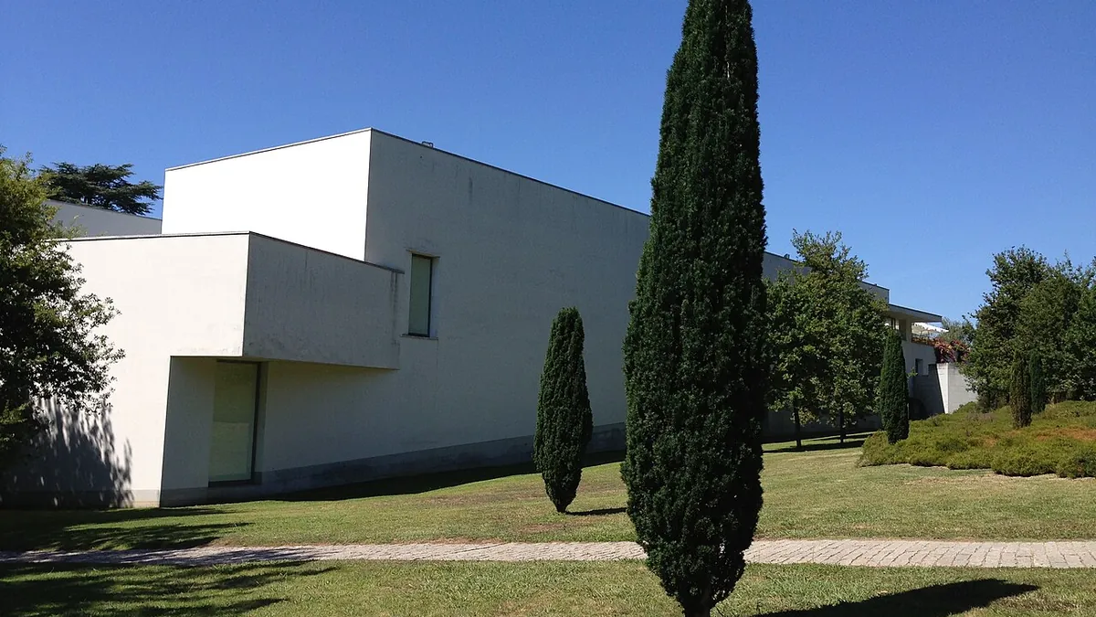 Fachada branca do Museu de Arte Contemporânea de Serralves vista do parque, com ciprestes ao lado