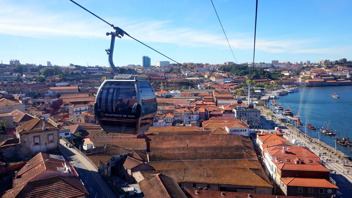 Cabine do Teleférico de Gaia suspensa sobre os telhados, com o Douro e o Porto ao fundo