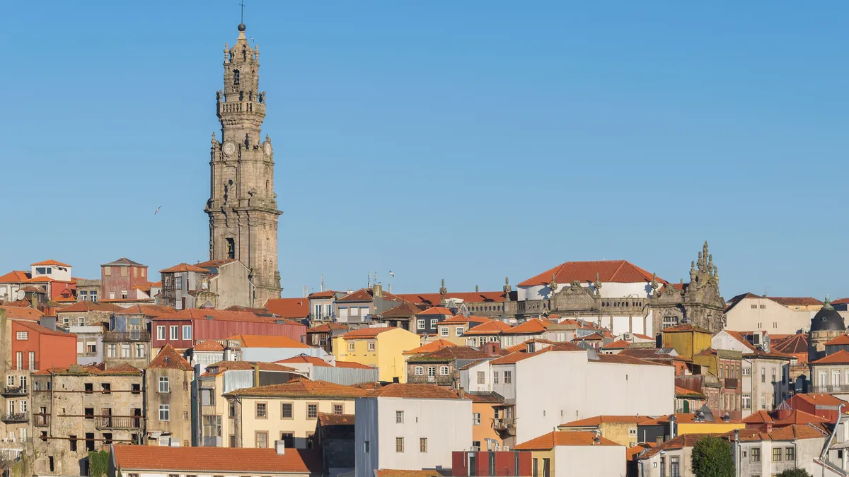 A Torre dos Clérigos erguida acima dos telhados de telha vermelha do centro do Porto, contra o céu limpo