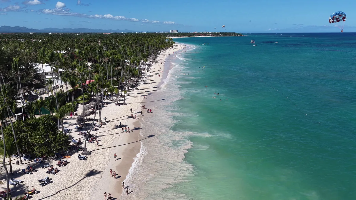 Faixa de areia da Playa Bávaro vista do alto, com o mar turquesa quebrando na praia e coqueiros na orla