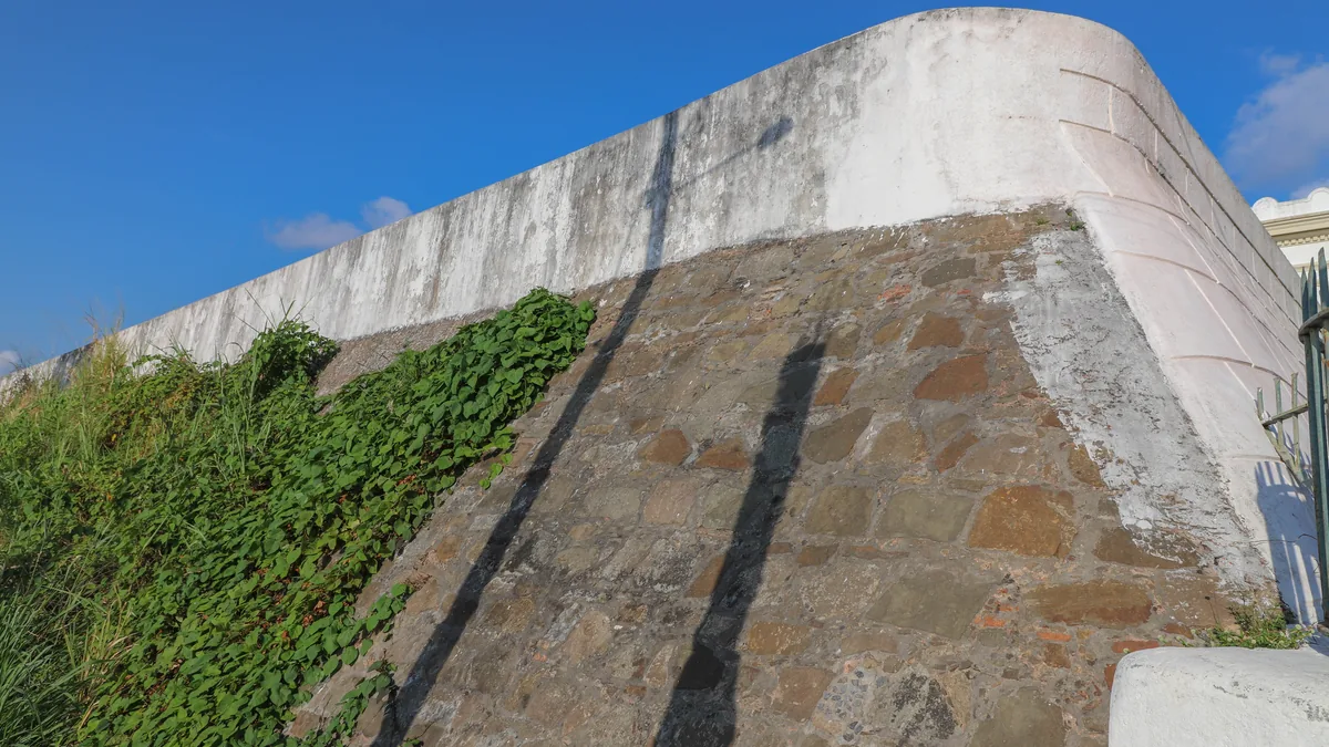 A muralha branca do Forte de Santo Antônio Além do Carmo, com vegetação subindo pela pedra da rampa