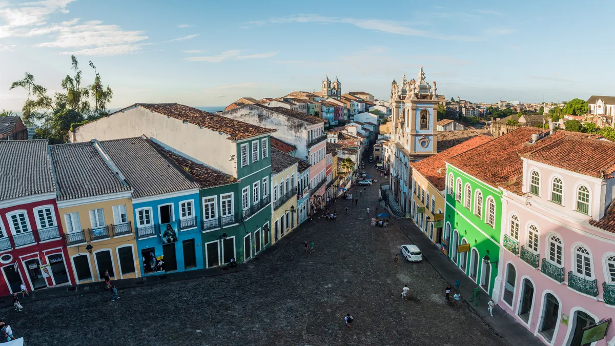 Vista do alto do Largo do Pelourinho, em Salvador, com as fachadas coloridas dos dois lados da ladeira de pedra, as torres da igreja ao fundo e o mar no horizonte
