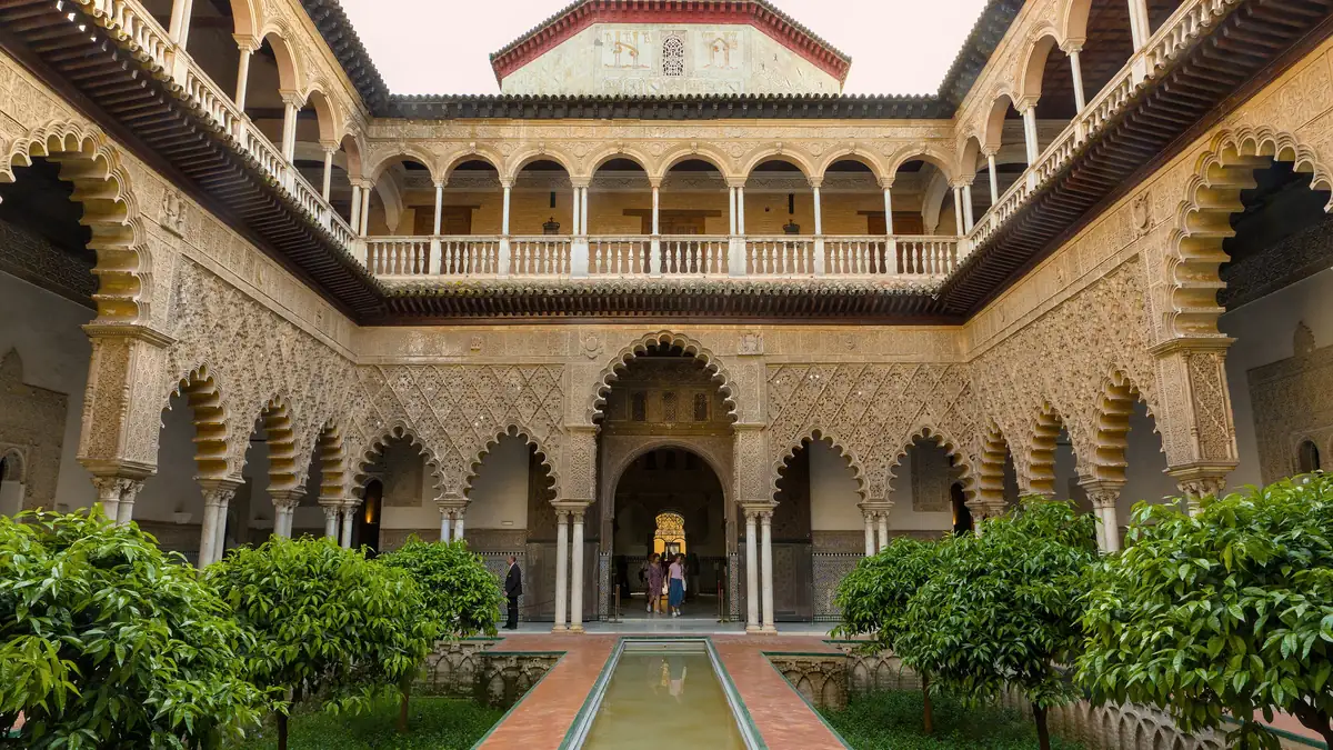 Patio de las Doncellas no Real Alcázar, com as arcadas rendilhadas em volta do espelho d'água e os canteiros rebaixados dos lados